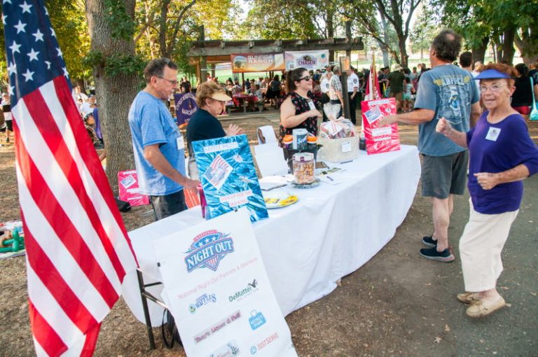 Kathy Morris, right, stands near a table set up at C-Bar-C Park on Aug. 2, for National Night Out. // M. Hazlip