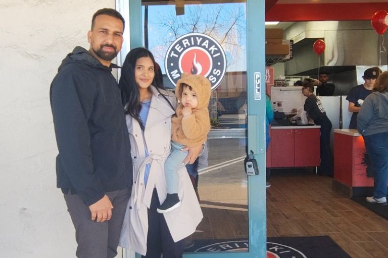 Teriyaki Madness Franchise owners Jas Deol and his wife, Amol, and their infant stand in front of their new restaurant on opening day, Jan. 17, 2025