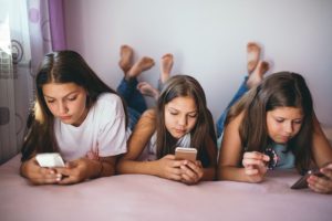 Stock photo. Three girls using social media from their phones. // Deposit photos