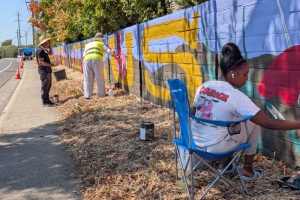 Muralist "Eres" stands with two community members helping to paint a community mural on a sound wall on Auburn Blvd. in Citrus Heights, Sept. 13, 2026.