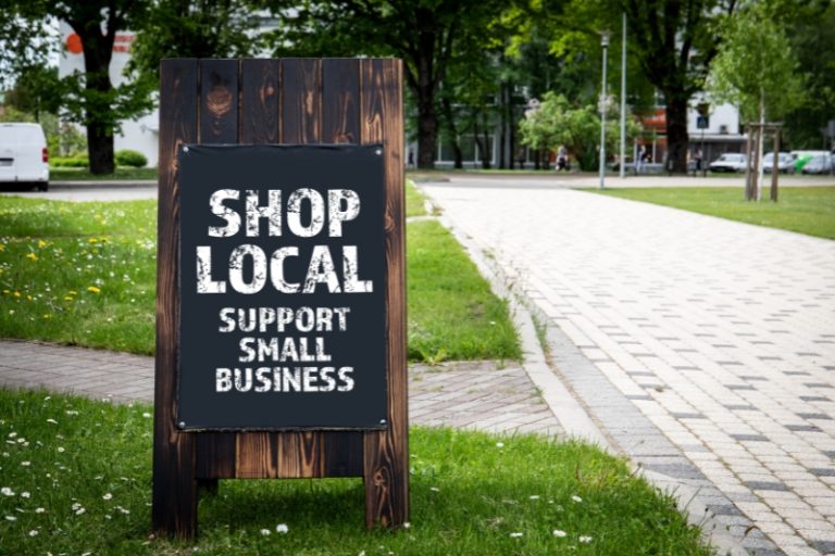A sign on a brick path: Shop local. Support small businesses. Stock photo.